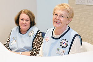 Two women wearing tunics that read 'Friends of Rockingham General  Hospital' sit at a desk.