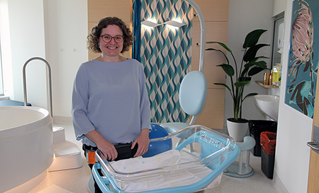 A woman stands besides a baby's crib in a birthing suite
