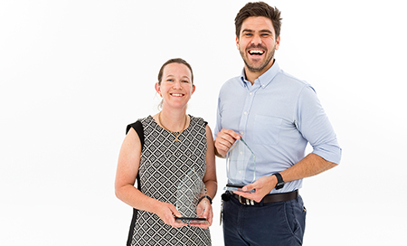 A woman and a man stand beside each other. Each is holding a small glass trophy.