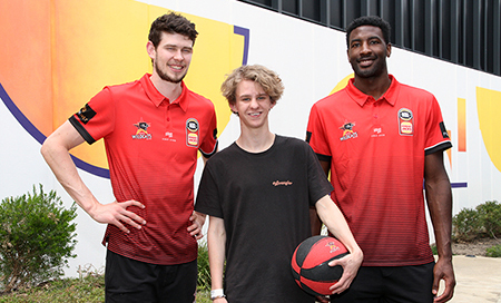 Two mean wearing Perth Wildcats team shirts stand with a teenage boy who holds a basketball.